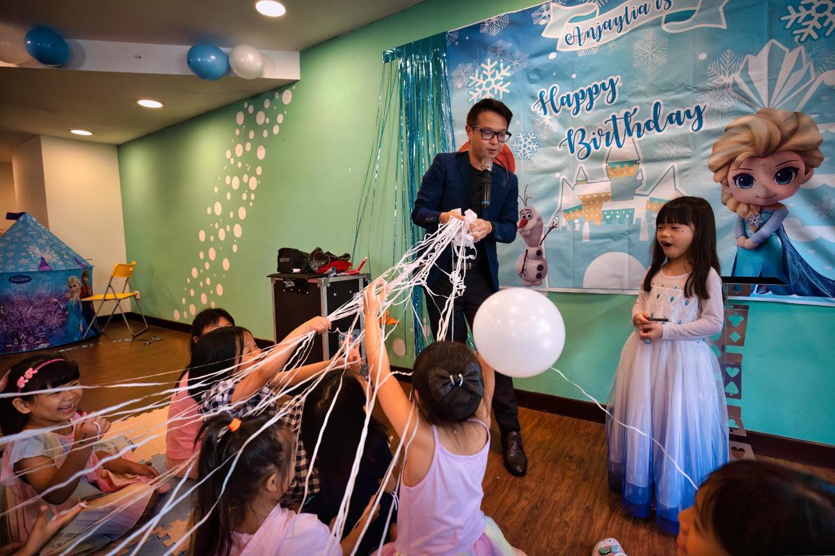 Children reaching towards paper streamers during a birthday magic show