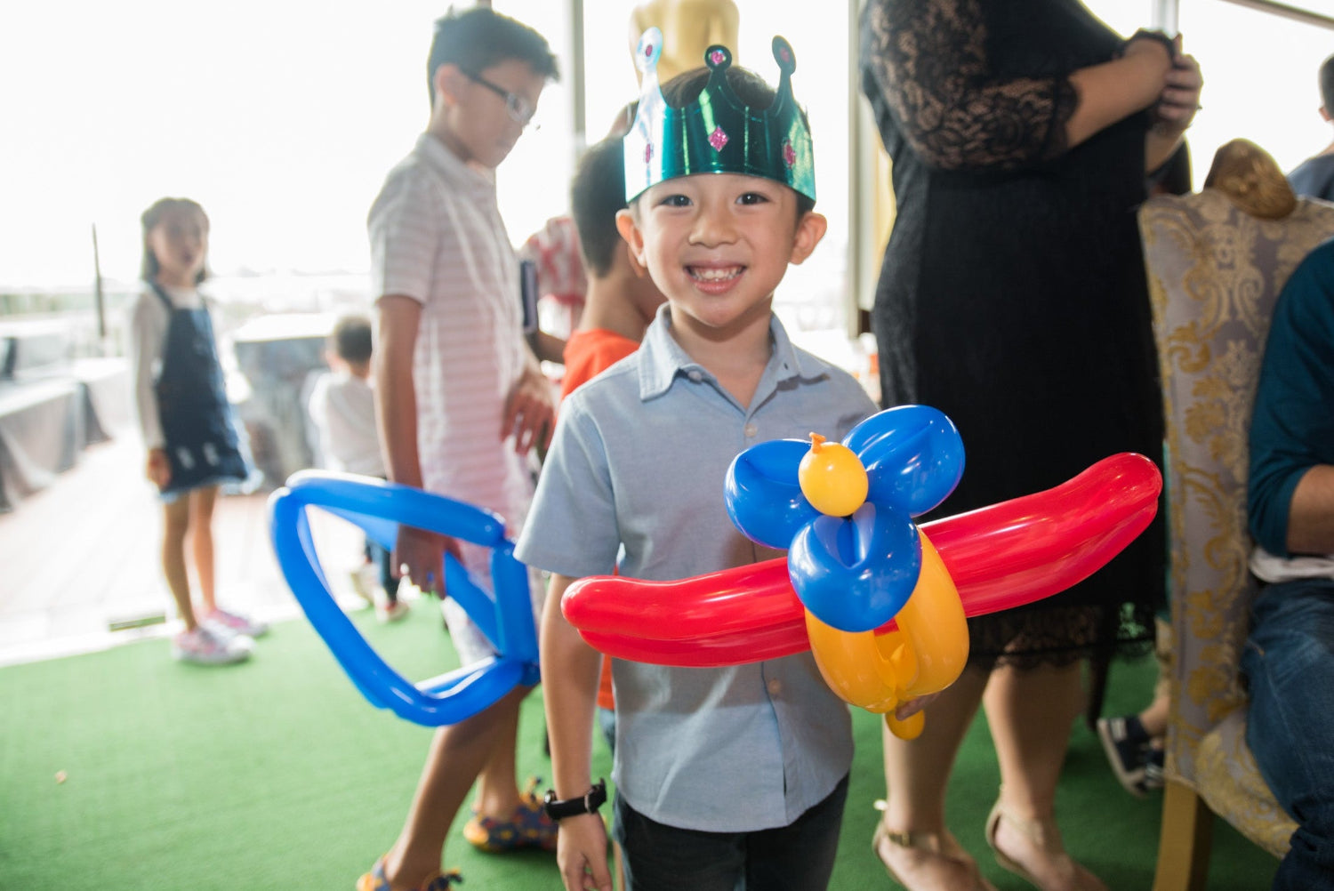 Smiling child wearing a  partyhat and holding a colourful balloon aeroplane