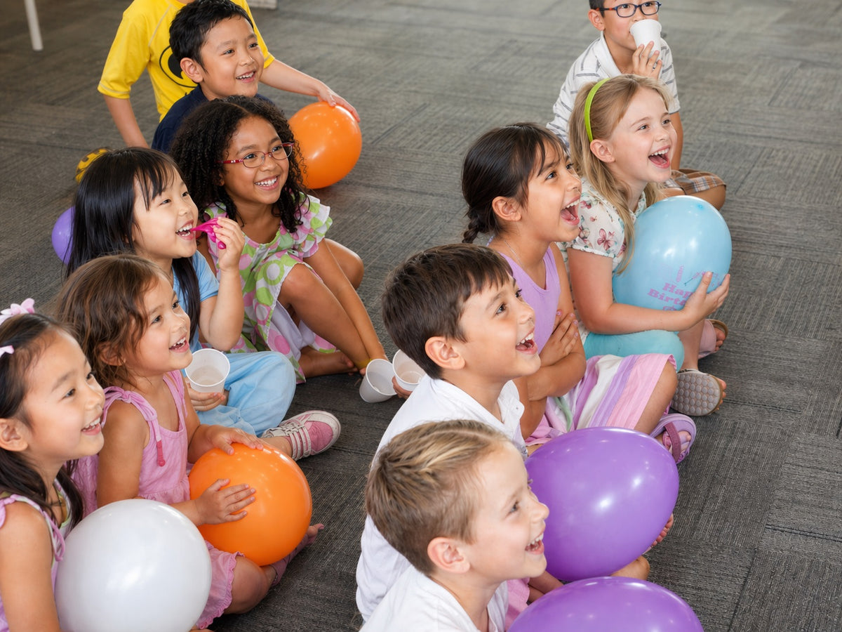 Children laughing together while holding balloons at a birthday party