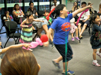 Children joining in a birthday party game while family and friends watch