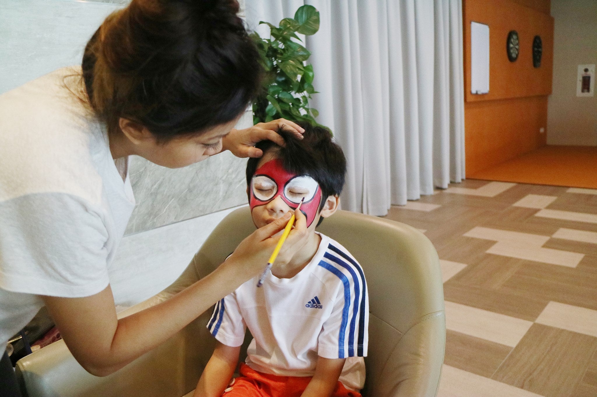 Face painter creating a red superhero mask design on a child’s face