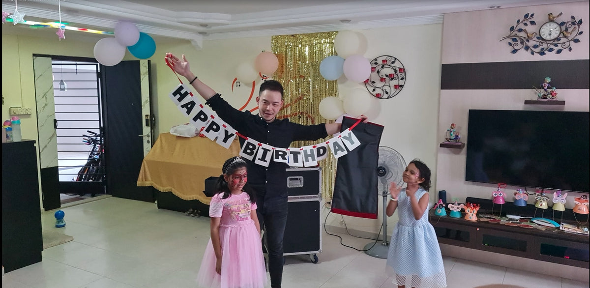 Magician holding a Happy Birthday banner with two children during the show